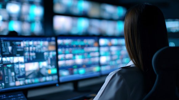 defense industry digital workplace plateforme collaborative sécurisée engineer monitoring digital systems inside Critical Infrastructure control room filled with multiple screens. Emphasizing cybersecurity, energy management and essential operations.